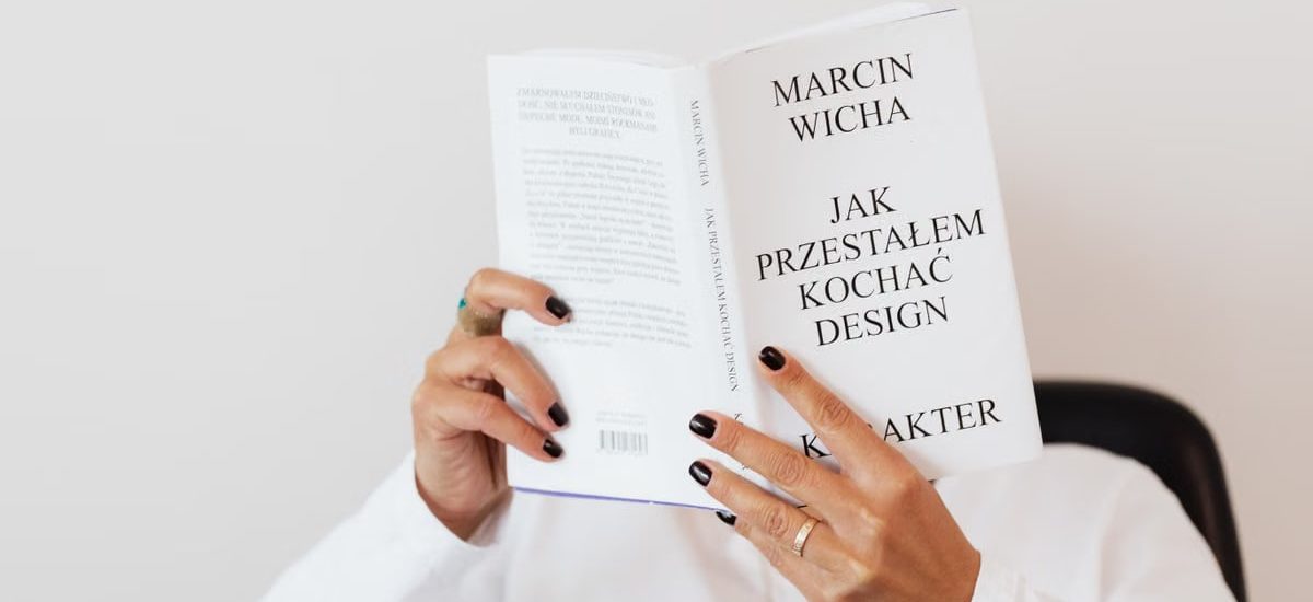 Anonymous female in white shirt with gold chain on neck reading interesting book covering face while sitting on black chair