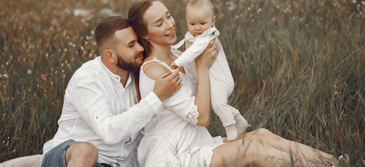 A joyful family with a baby relaxing outdoors in a field during summer.